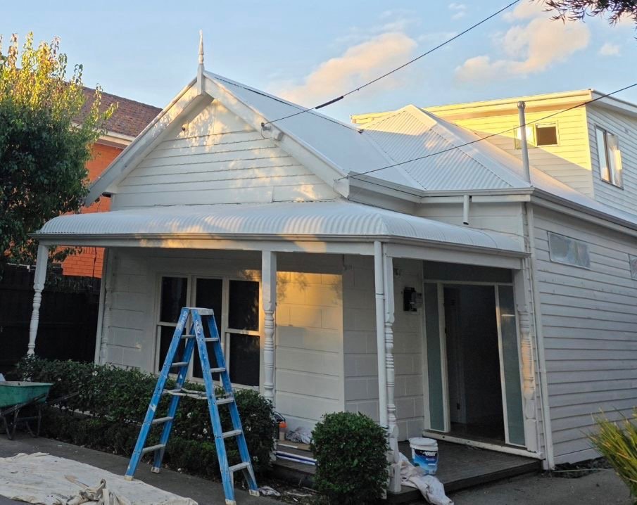 After exterior house repaint photo showing the same weatherboard home finished in fresh white paint